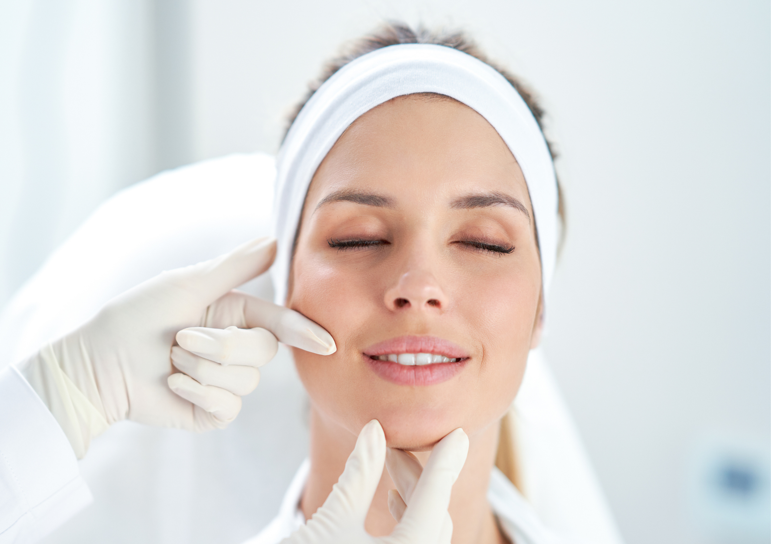 Close-up of a clinician in gloves lifting a woman's chin during a cosmetic facial treatment.